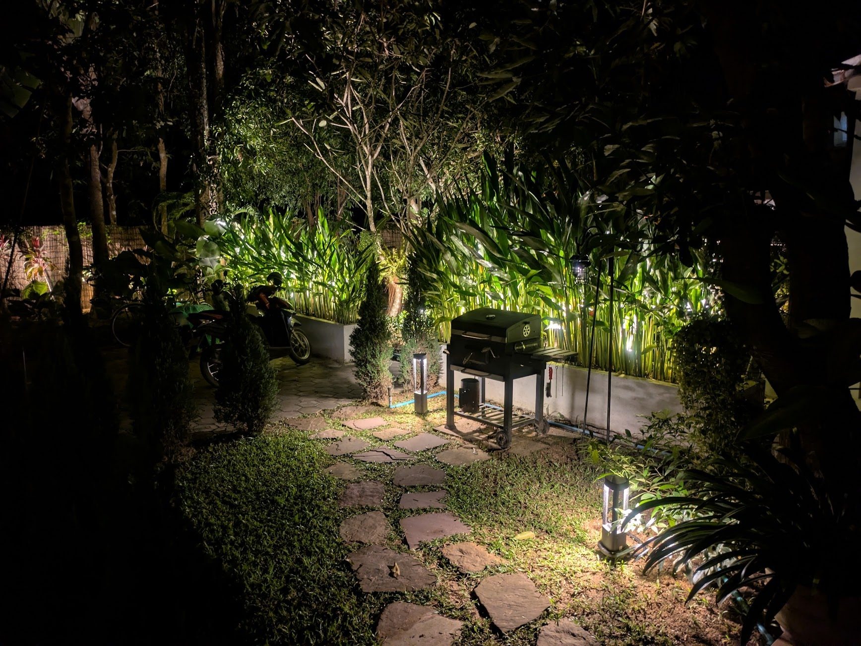 A garden patio at night: grill, bollard lights and a wall-washed plant bed
